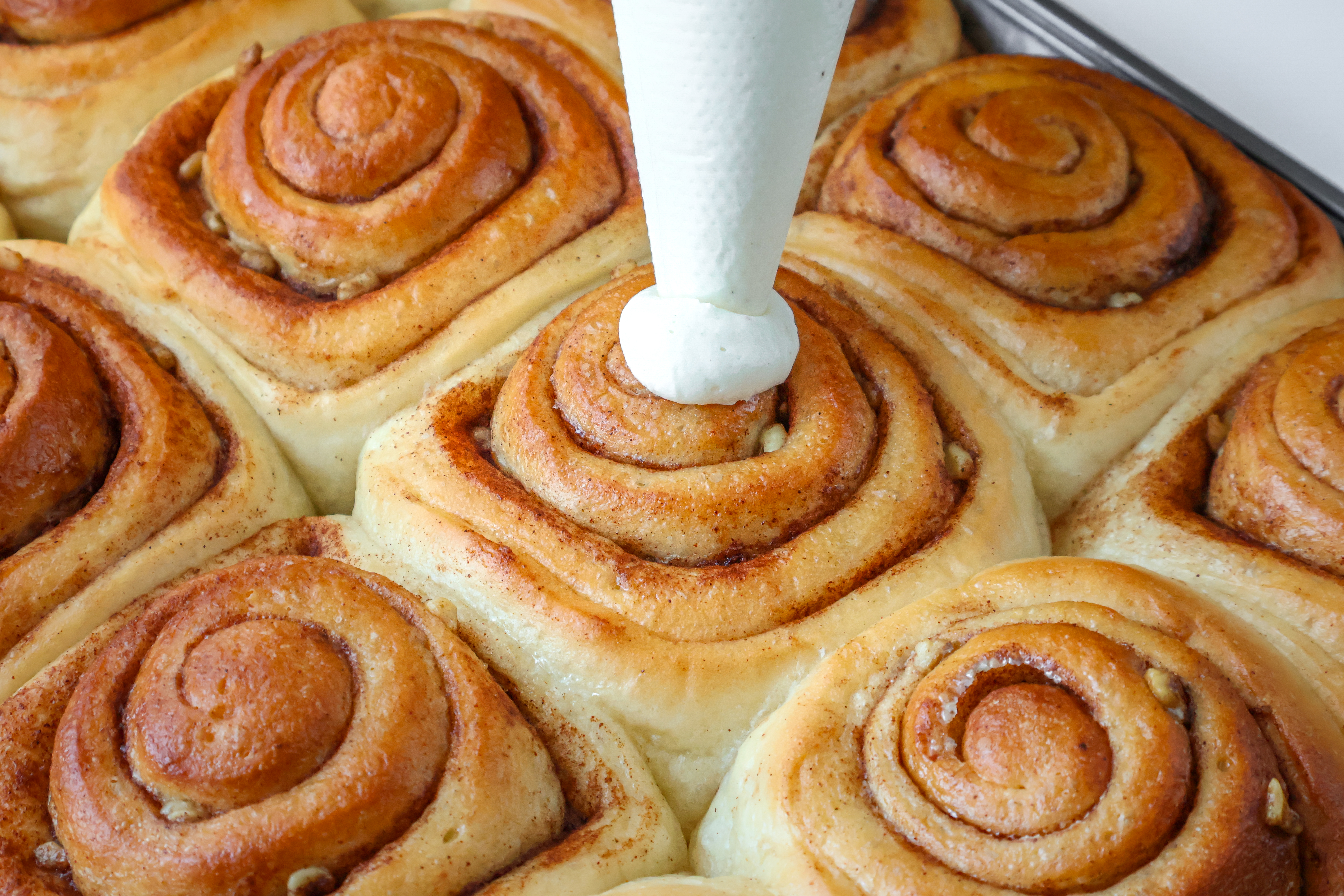 Baker adding frosting to cinnamon rolls
